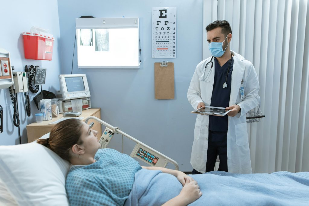 Doctor wearing face mask consulting with a patient in a hospital room, highlighting healthcare safety.