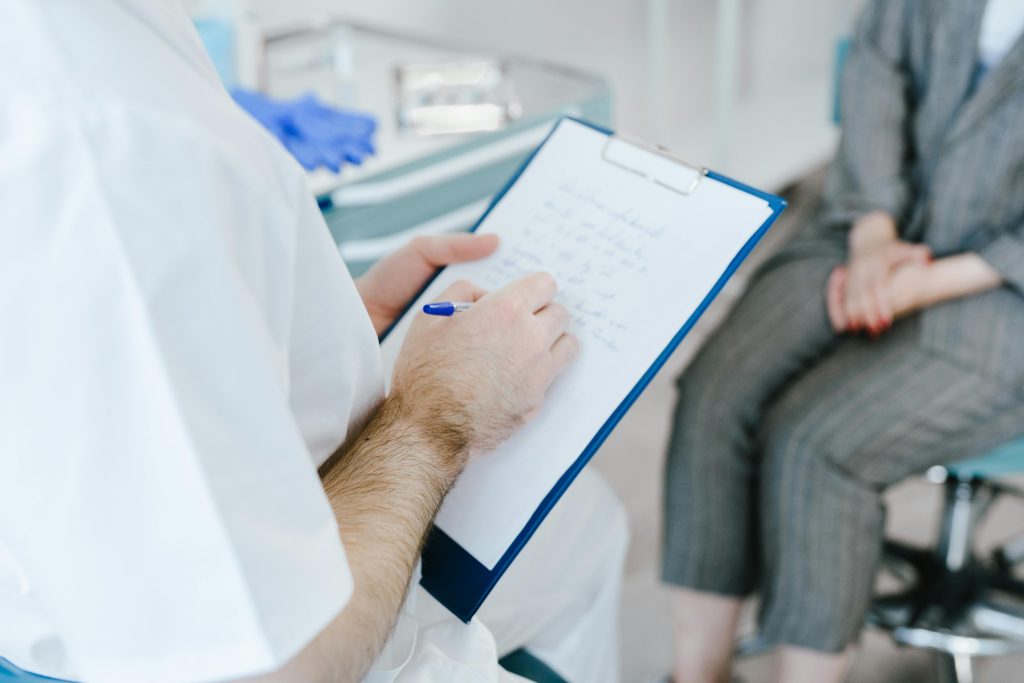 Medical professional writing patient notes on clipboard during consultation.